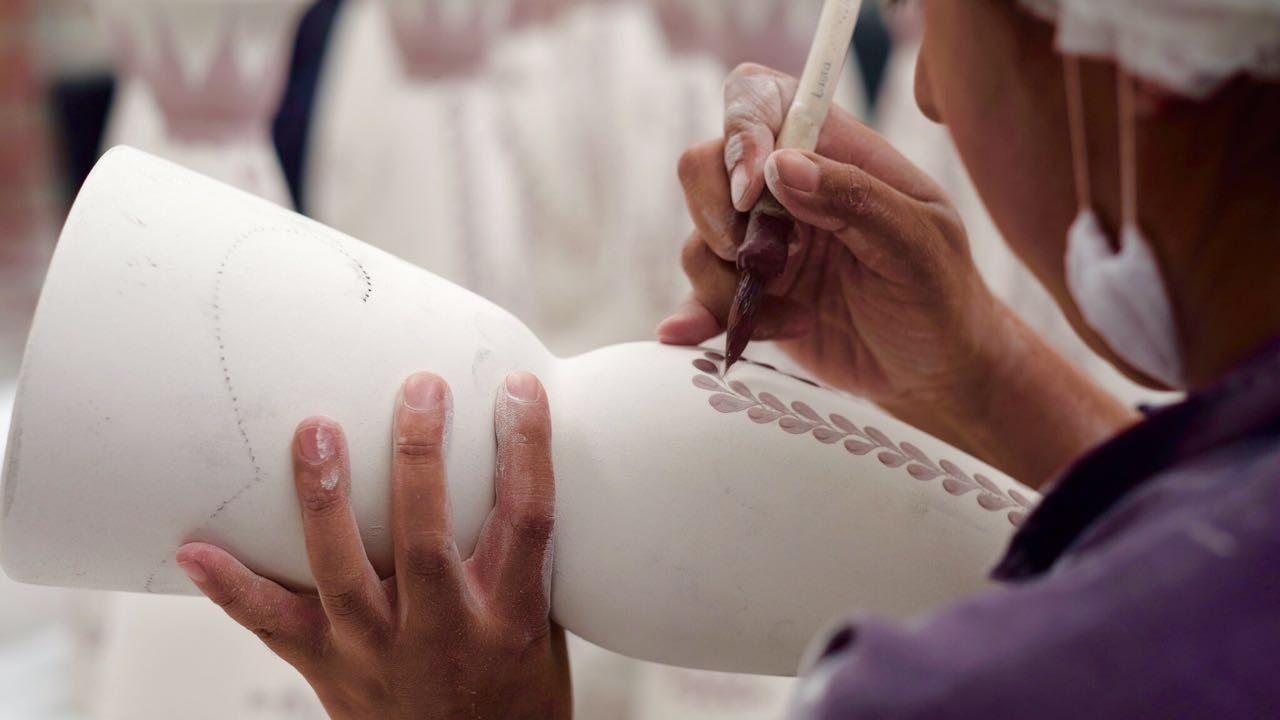 A woman panting a pattern on a ceramic vase